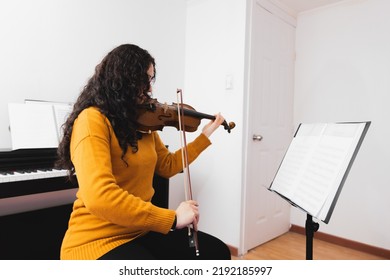 Brunette Woman Wearing A Yellow Sweater, And Playing Violin By Reading Sheet Music.