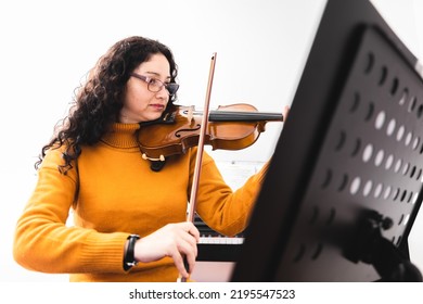 Brunette Woman Wearing A Yellow Sweater, And Playing Violin By Reading Sheet Music.