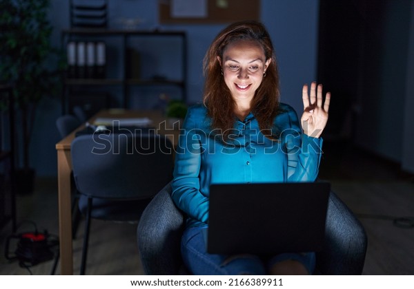 Brunette woman working at the office at night showing\
and pointing up with fingers number four while smiling confident\
and happy. 