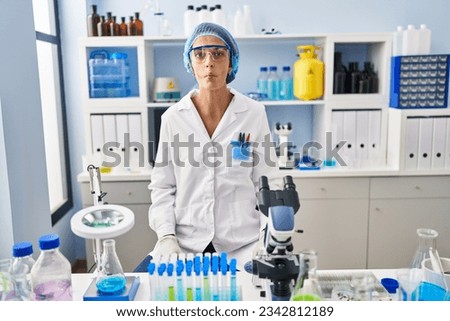 Brunette woman working at scientist laboratory making fish face with lips, crazy and comical gesture. funny expression. 