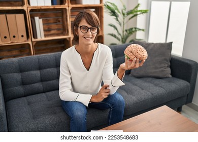 Brunette woman working at therapy office holding brain looking positive and happy standing and smiling with a confident smile showing teeth  - Shutterstock ID 2253548683