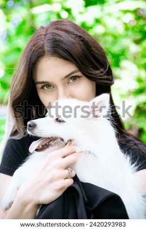 Brunette young girl in black clothes walking in the green par with a white pomeranian funny dog