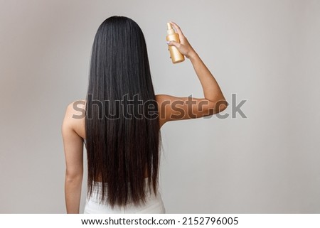 Brunette young woman applying hair spray on hair