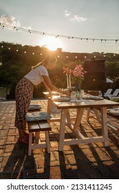 Brunette Young Woman Arranging Dining Table And Putting Cutlery On It In The Backyard. Everything Is Prepared For Family Gathering