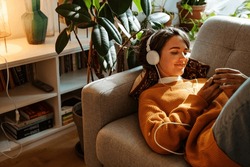 Brunette Young Woman Listening Music And Using Cellphone While Resting On Couch At Home