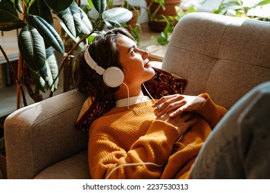 Brunette young woman listening music while resting on couch at home