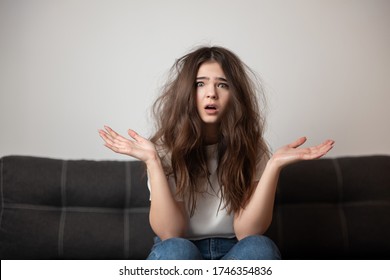 brunette young woman with tangled long hair looks desparate and unhappy with her hairstyle, bad hair day concept