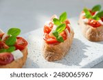 Bruschetta with cherry tomatoes, mozzarella cheese and basil in sun rays on marble board. Traditional Italian appetizer, snack or antipasto. Vegetarian food. Healthy eating. Mediterranean food.
