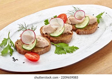 Bruschetta With Pate, Cucumber And Radish, Garnished With Herbs And Tomatoes On A Beautiful White Oval Plate. View From Above. 