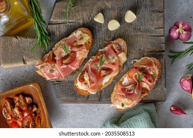 Bruschetta with prosciutto, hard cheese, tomatoes, herbs and spices on a wooden board. Tasty breakfast.