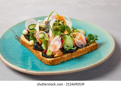 Bruschetta with salmon, cream cheese and vegetables on blue ceramic plate. Toast with salmon contemporary style. Salmon bruschetta in modern ceramic dishware. Handmade dinner plate
