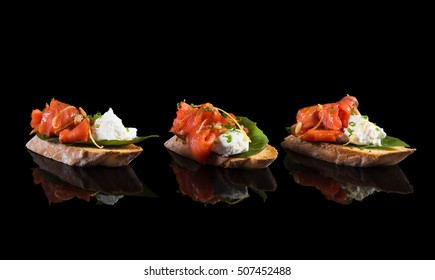 Bruschetta with salmon and soft cheese on black background