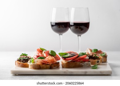 Bruschetta set with prosciutto and basil, tomatoes and mozzarella, camembert and berries, mushrooms and parsley on marble board. Antipasto open sandwich appetizer