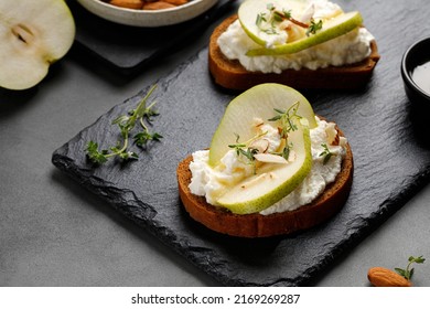 Bruschetta, snack, appetizers. Toast with cottage cheese ricotta cheese, pear, honey and almond. Sandwiches on slate board and dark background.