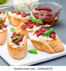 Bruschetta with sun dried tomato, feta and philadelphia cheese and basil on a ceramic plate, square format