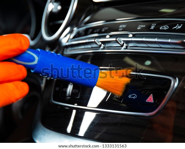 Brush cleaning off dust from the car interior\
details, control panel of the dashboard. A man cleaning car with\
cloth and brush. Car detailing.  Worker cleaning. Brush and\
cleaning solution to\
clean
