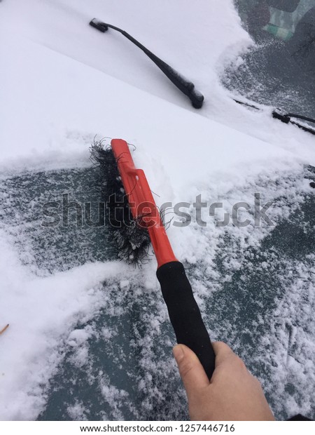brush cleans the car from snow on the\
background of the car parts. Wipers, headlights, hood in the snow.\
Winter snowfall and\
snowstorm\
