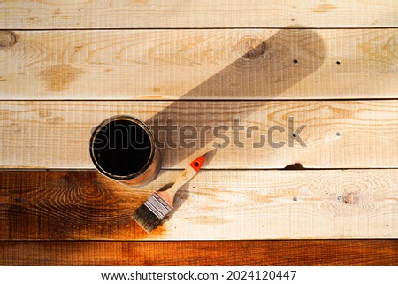 Brush for covering wood and varnish in a jar on a wooden surface. Protecting wood from water, varnishing floors, furniture, carpentry.