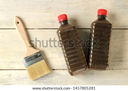 A brush lies next to a plastic bottle with varnish on an old white vintage wooden plank table. Place for text or logo.