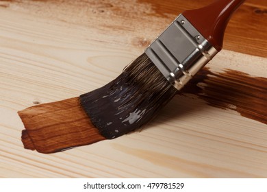 Brush on can of brown paint on partly painted wood, close up, low focus