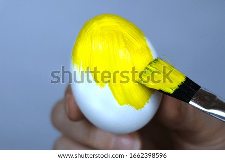 Brush painting an Easter egg with yellow paint. Getting ready for Easter. Selective focus. Close-up