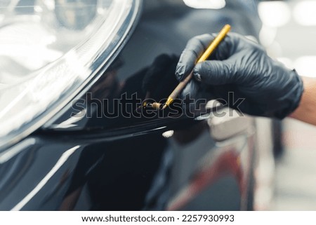 Brush painting over small scratches. Car detailing process. Professional male mechanic in protective gloves using car detailing equipment to touch up car paint. High quality photo