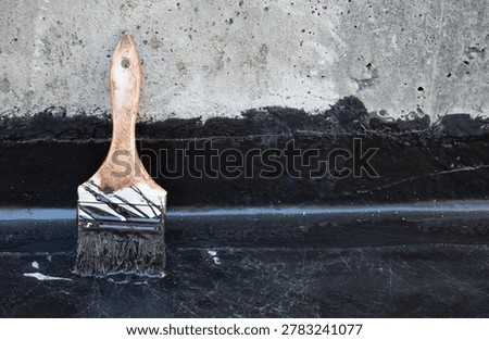 Brush used for liquid membrane application. Close up. Fluid applied liquid coating on concrete floor with vertical upturn detail. Exterior leak repair on balcony, patio or foundation. Selective focus.