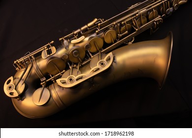 A Brushed Brass Tenor Saxophone With An All Black Background.