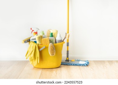 Brushes, bottles with cleaning liquids, sponges, rag and yellow rubber gloves on white background. Cleaning supplies in the yellow bucket on the wooden floor. Cleaning company service advertisement - Powered by Shutterstock