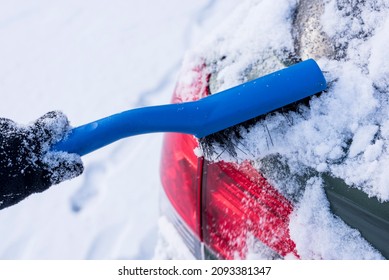 Brushing fresh snow off taillight with scraper during cold winter.