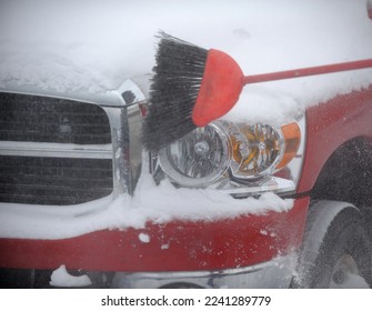 brushing snow off front headlights of red truck with red broom in winter driving hazards and winter preparation or winter driving in snow horizontal format room for type winter driving conditions  - Shutterstock ID 2241289779