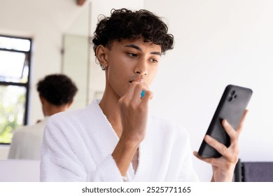 Brushing teeth, young young man in bathrobe using smartphone in bathroom. Hygiene, morning routine, grooming, technology, multitasking, self-care - Powered by Shutterstock