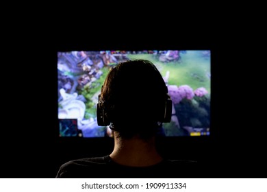 Brusque, Brazil - February 03 2021 - Dota. Young Man Silhouette With Headphone Playing Video Game. The New Game On A Screen In Front Of Him