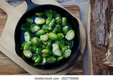       Brussel Sprouts In A Cast Iron Pan Atop A Wooden Pizza Peel, Cutting Board, And Wood Log                         