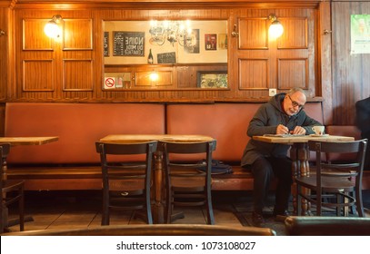 BRUSSELS, BELGIUM - APR 2: Older Man Alone Writing Letter Inside Old Bar Of Cafe With Historical Interior And Evening Light On April 2, 2018. More Than 1,200,000 People Lives In Brussels