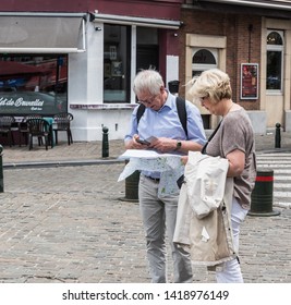 Brussels Old Town / Belgium - 06 07 2019: Elderly Couple Looking At A Tourist Map And A Smartphone, Searching For Directions