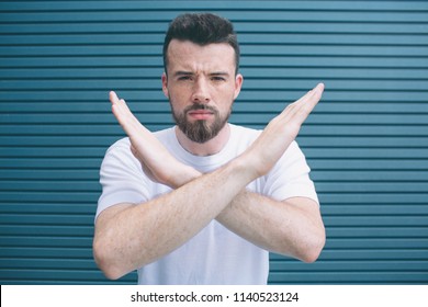 Brutal And Angry Man Is Standing With Hands Crossed And Looking At Camera. He Is Not Happy. Isolated On Striped And Blue Background.