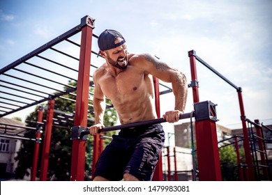 Brutal athletic man making pull-up exercises on a crossbar at outdoor streeet gym.