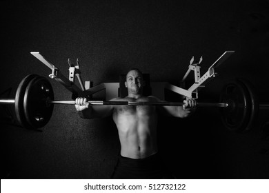 Brutal Athletic Man Pumping Up Muscles On Bench Press In Monochrome. Bodybuilder. Naked To The Waist. Black And White Photography. Sport. Low Key. Gym. Isolated On Black.