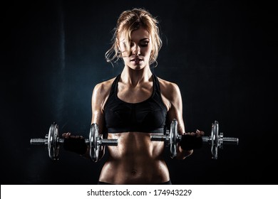 Brutal athletic woman pumping up muscules with dumbbells
