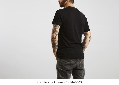 Brutal attractive bearded biker man with tattooed hands poses backside in black blank t-shirt from premium thin cotton, isolated on white mockup