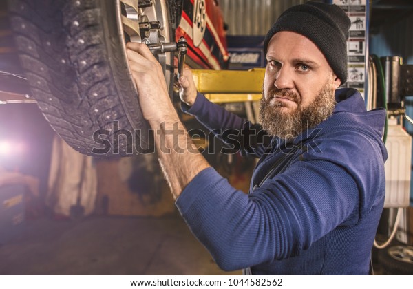 Brutal bearded car mechanic works in the\
garage. A tire fitting\
mechanic.