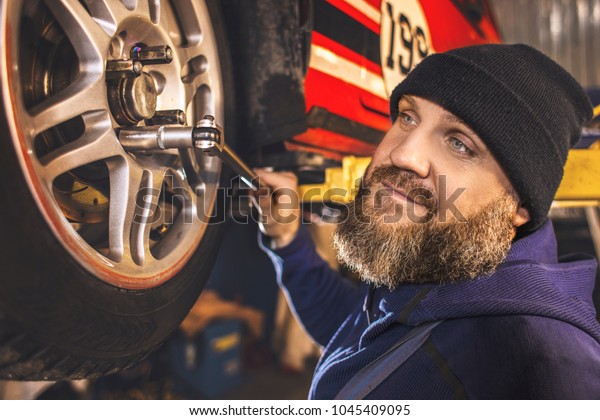 Brutal bearded car\
mechanic works in the garage.The master is repairing the car.\
Repairman in the garage.