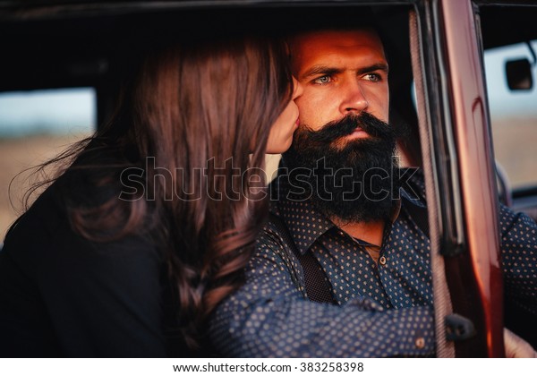 brutal\
bearded man with a mustache in a shirt, pants with suspenders with\
a girl with dark hair and big lips with bright red lipstick in a\
short dress and heels near retro car at\
sunset