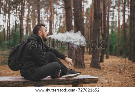 brutal bearded young man having rest in forest and vaping vape device. Lifestyle. Vape concept . Rest in forest Stock photo © 