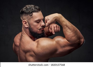 Brutal Bodybuilder With Black Beard And Mustache Points To His Huge Biceps In Gray Background.