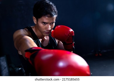 Brutal boxer fighter, confident young athlete asian man in red boxing gloves, punching a sand bag in professioal gym. Sportsman muay thai boxer work out, training, fighting in gloves.