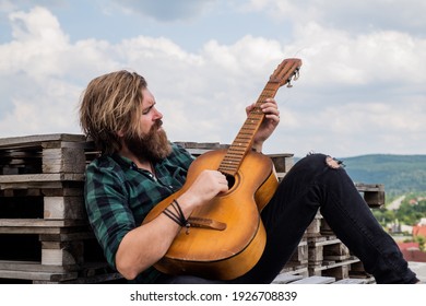 brutal caucasian hipster with beard in shirt play acoustic guitar, music.