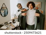 Brutal curly haired model trying on new suit while tailor assisting him