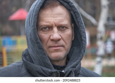 Brutal Handsome Man, Middle-aged, 55-60 Years Old, Stands In The Park In A Gray Sweatshirt With A Hood On His Head